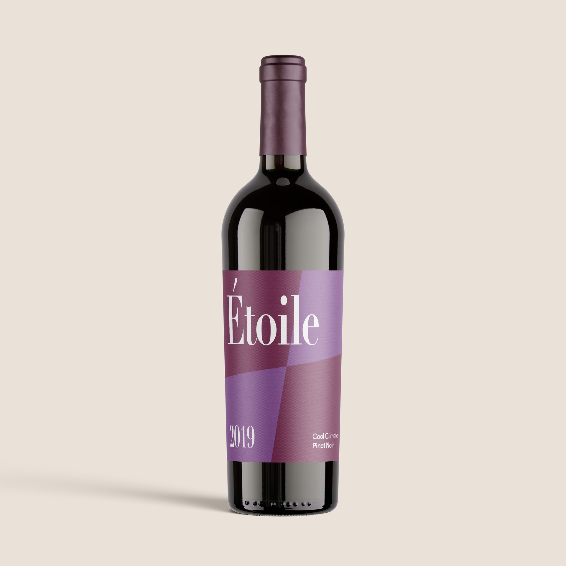 Garrafa de vinho escura inclinada com rótulo roxo sobre fundo bege