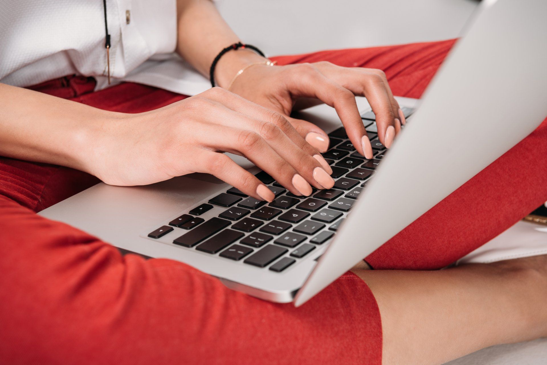 A woman is typing on a laptop computer while sitting on the floor
