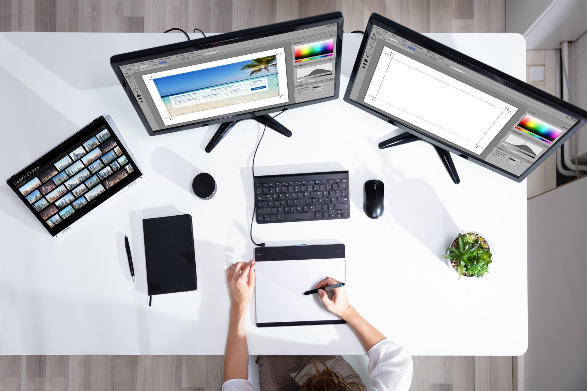A person is sitting at a desk with two monitors and a tablet
