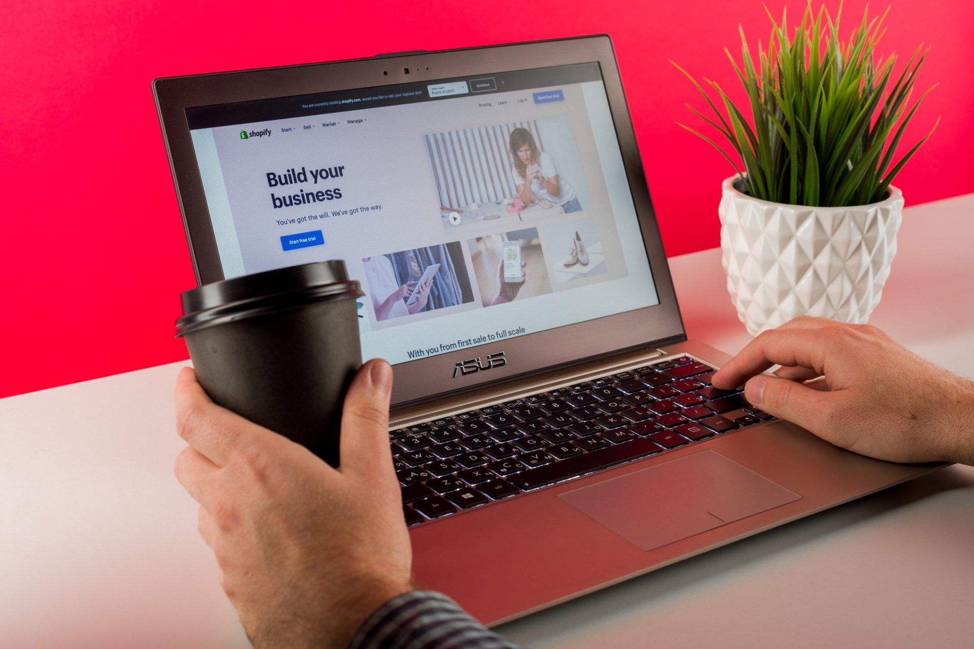 A person is typing on a laptop while holding a cup of coffee
