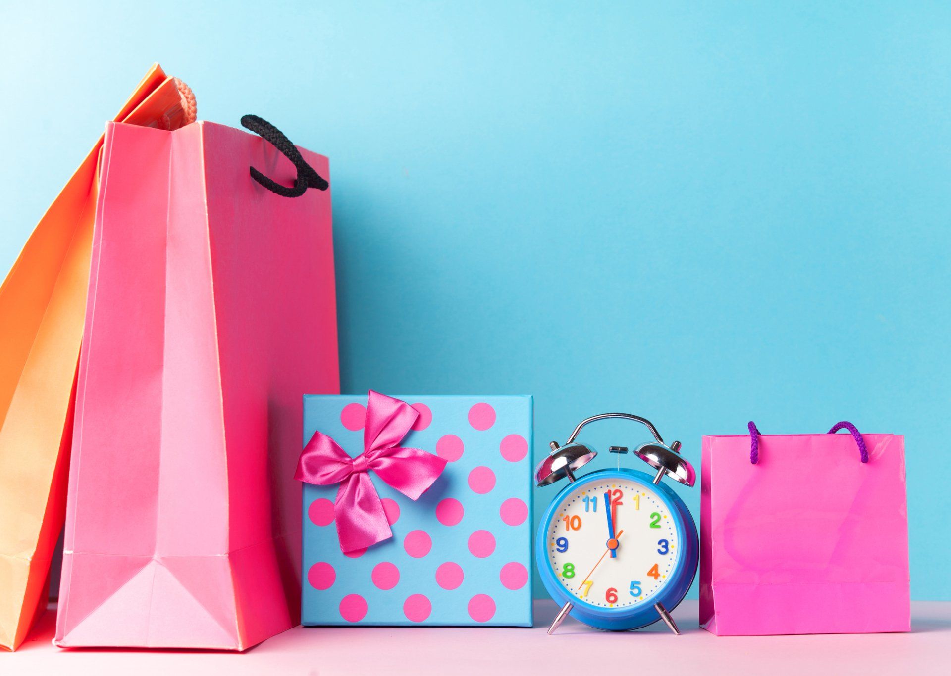 A blue alarm clock sits between two pink shopping bags