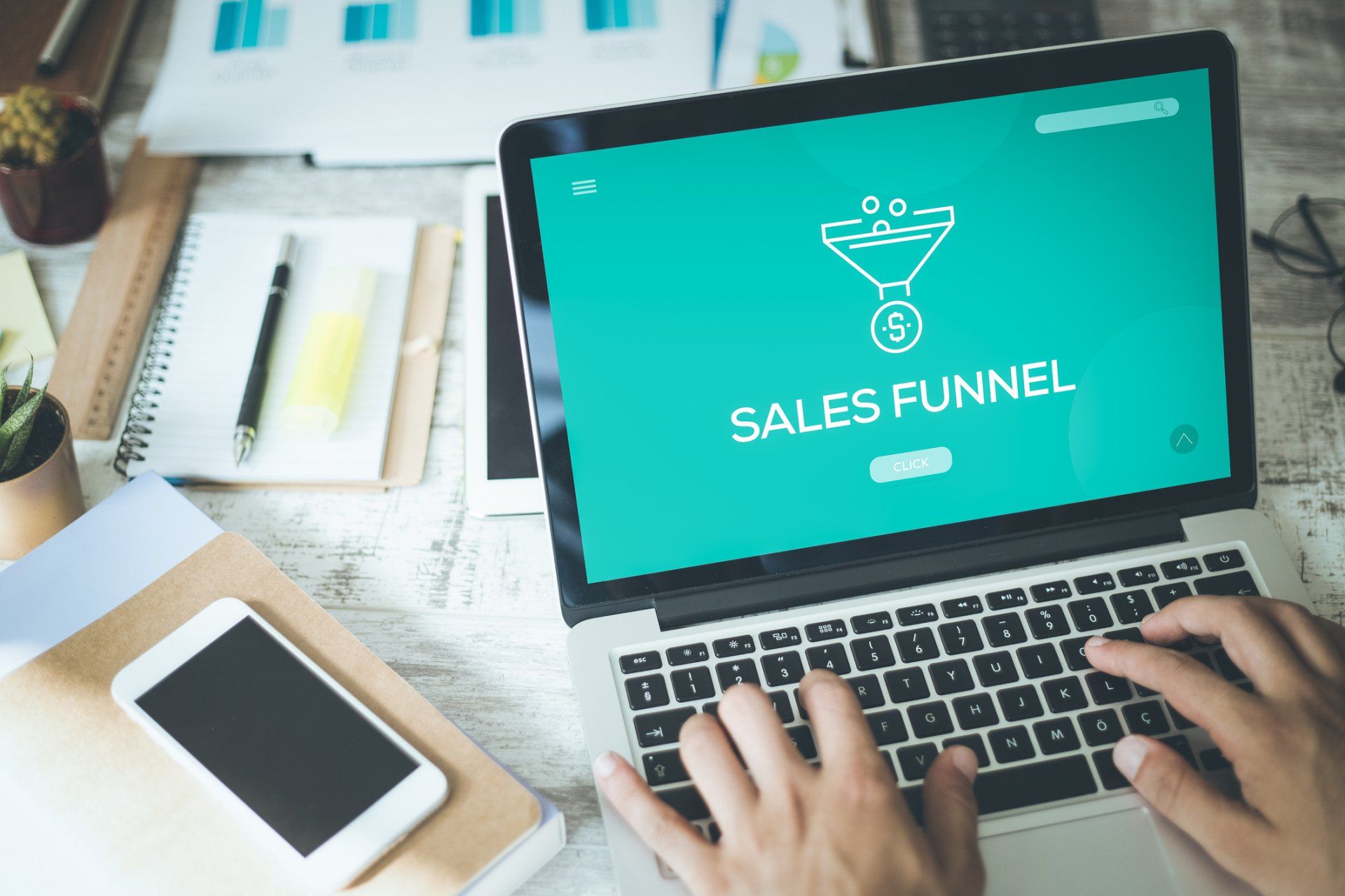 A person is typing on a laptop with a sales funnel on the screen
