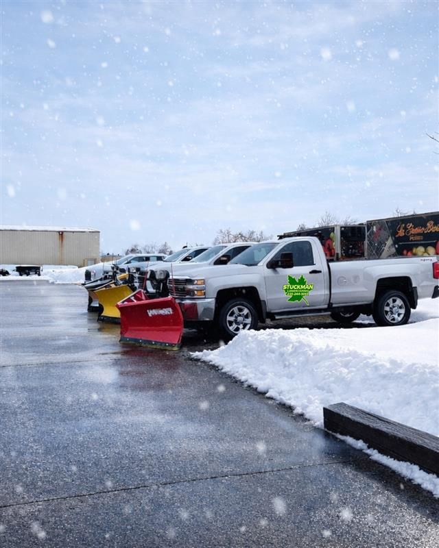 White pickup with red snowplow parked in a snowy lot during snowfall