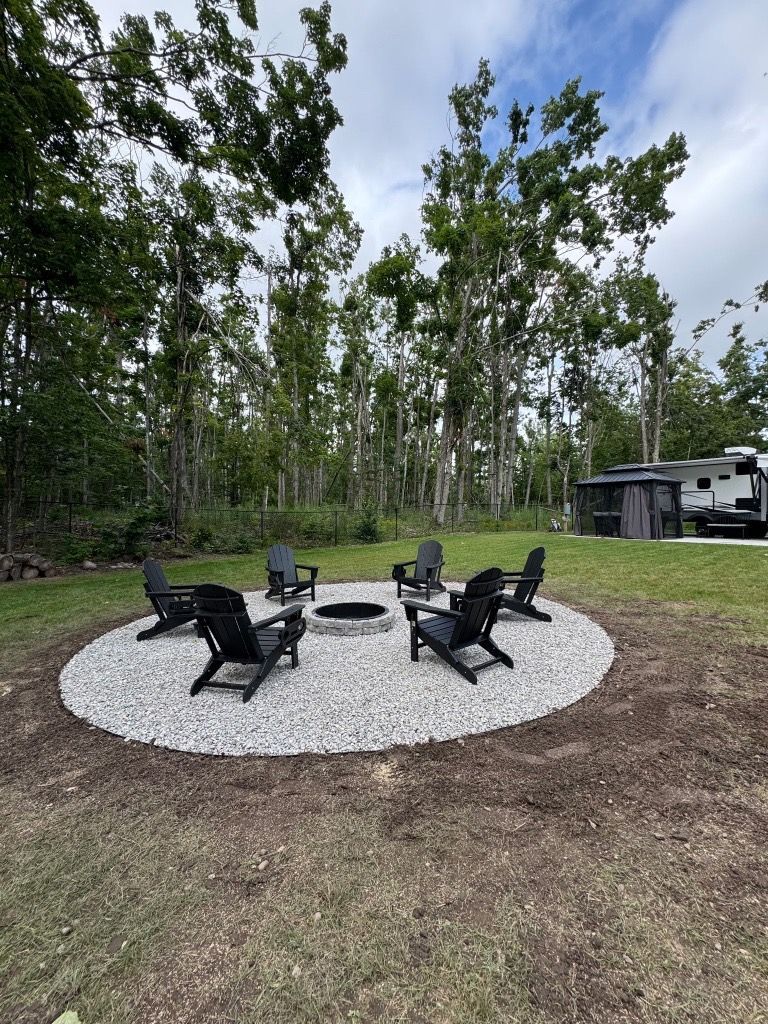 Fire pit seating area with black chairs on a white gravel circle in a wooded yard