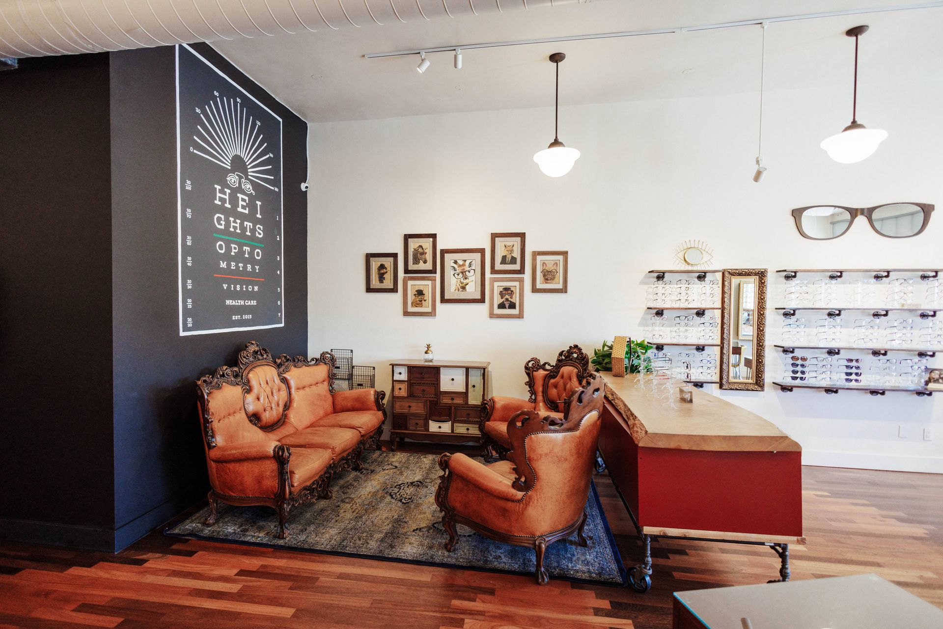 A waiting area in an eyewear shop featuring two vintage leather sofas, a patterned rug, framed art, and a sales counter.