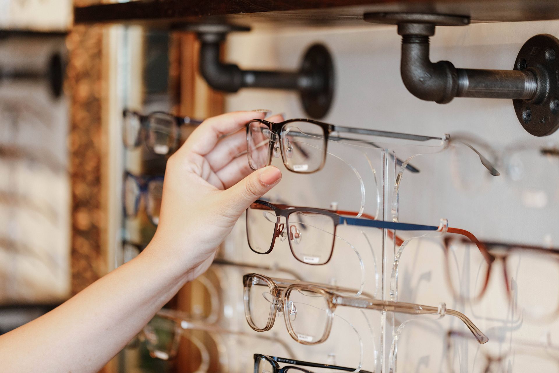 A hand picks a pair of glasses from a display rack in an optical shop.