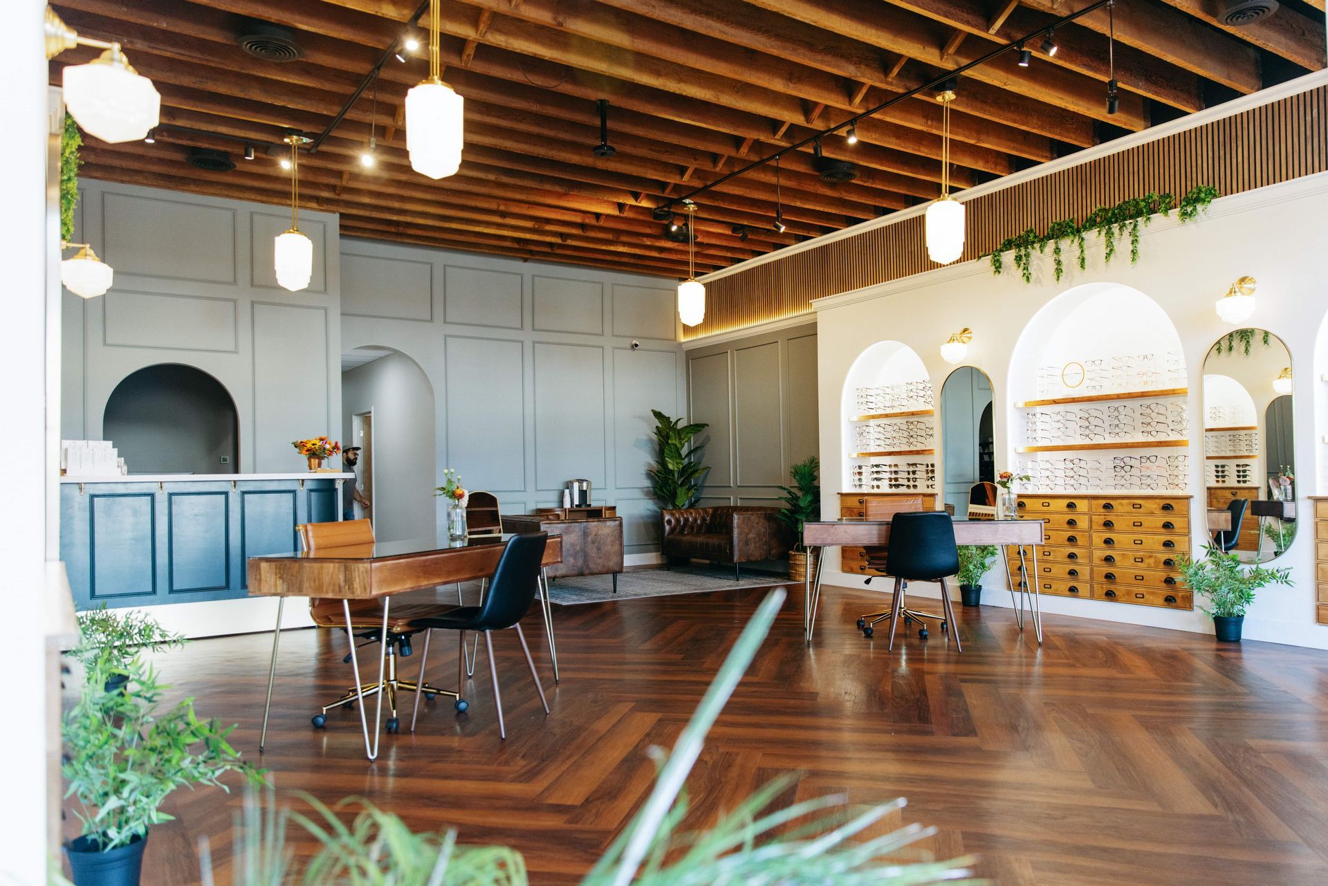 A modern retail space with wood floors, exposed ceiling beams, a blue service desk, and arched shelving displays.