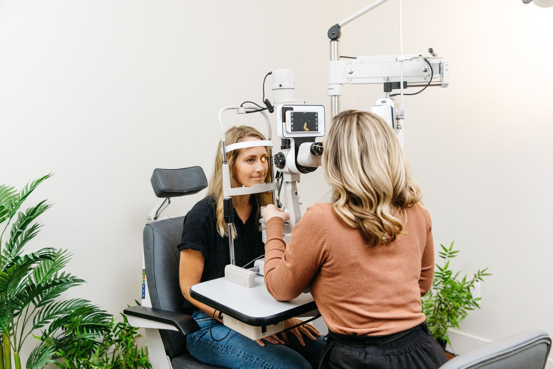 A person having an eye exam with a slit lamp machine, with an optometrist assisting them in a brightly lit office.