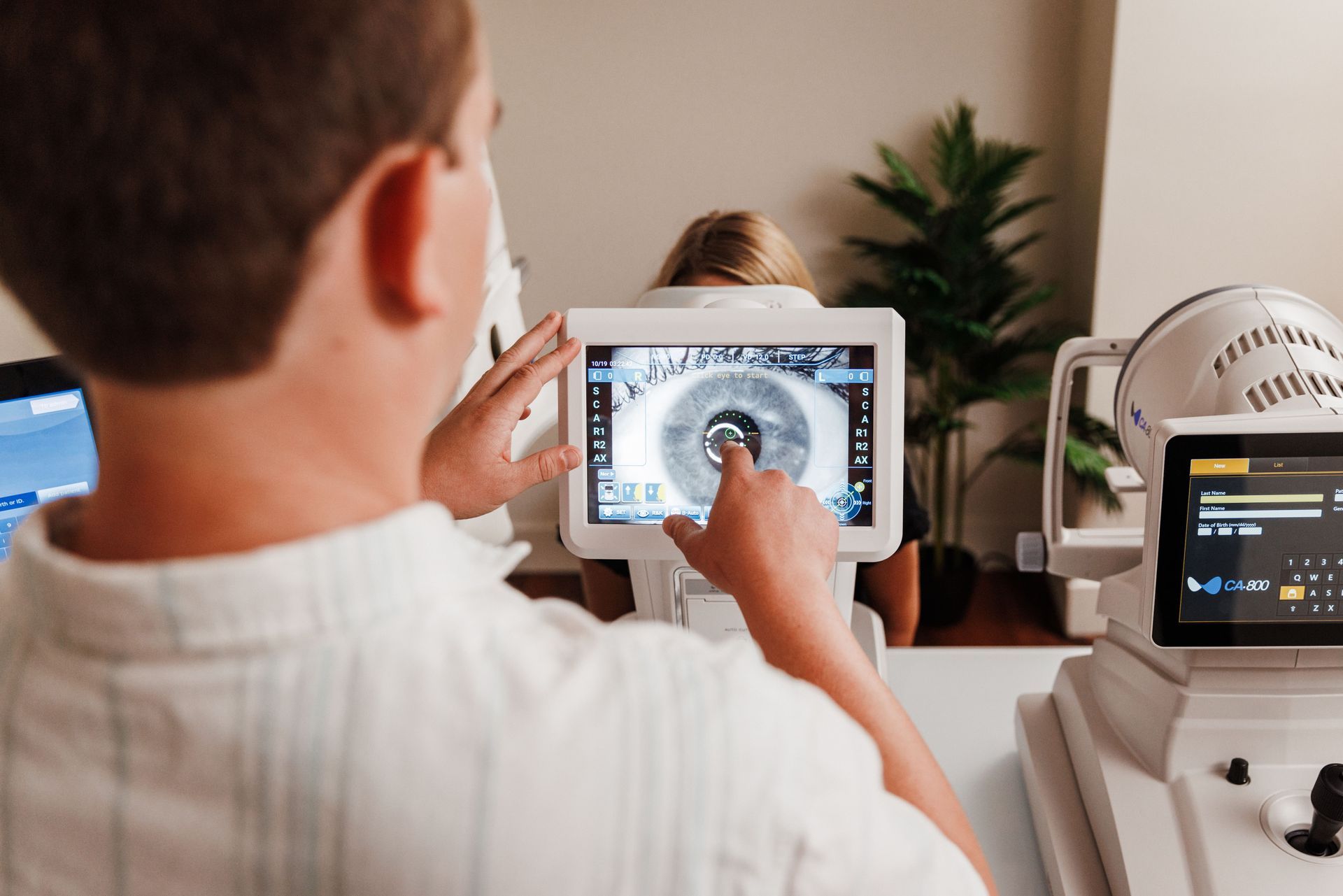 An optometrist points to a digital screen showing a patient's eye scan during an eye exam in a clinic.