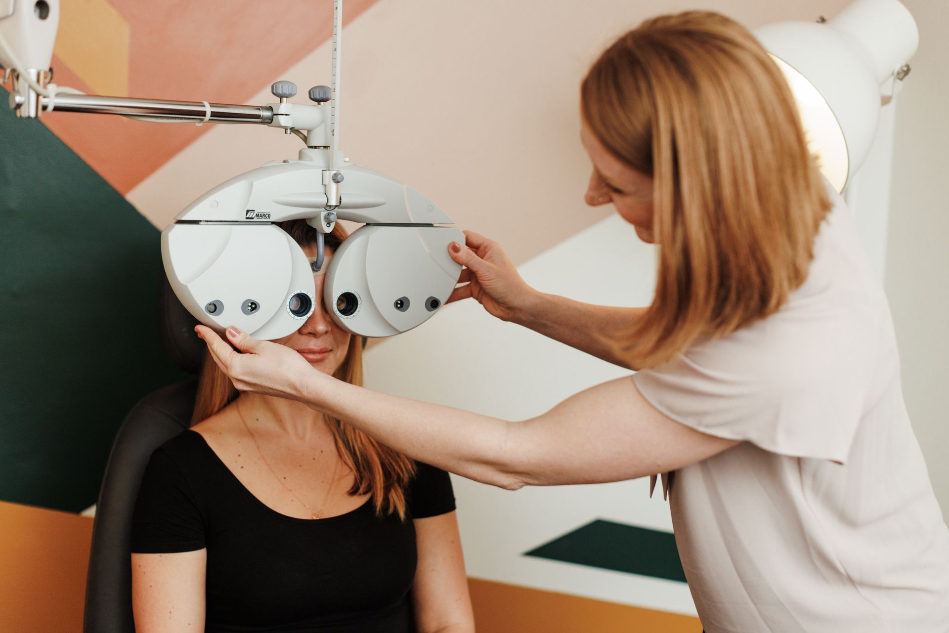An optometrist adjusts a phoropter in front of a patient during an eye examination.