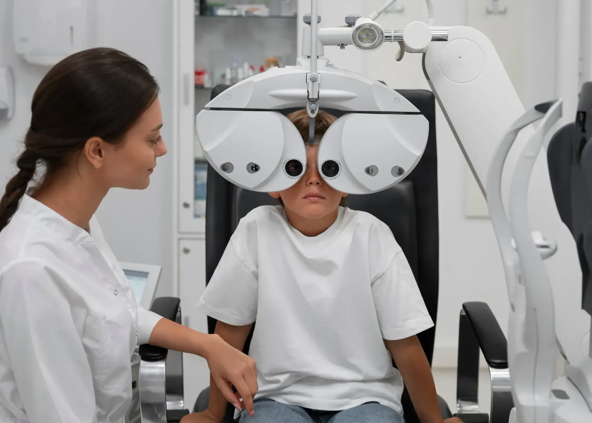 A patient undergoes an eye examination with a phoropter while an optometrist assists in a clinical setting.
