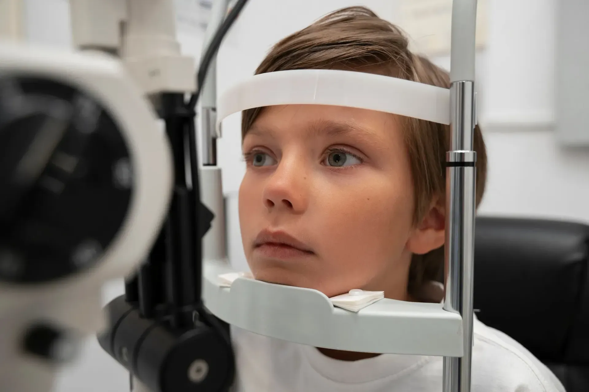 A child sits at an eye exam machine with their chin and forehead resting on the support frame.