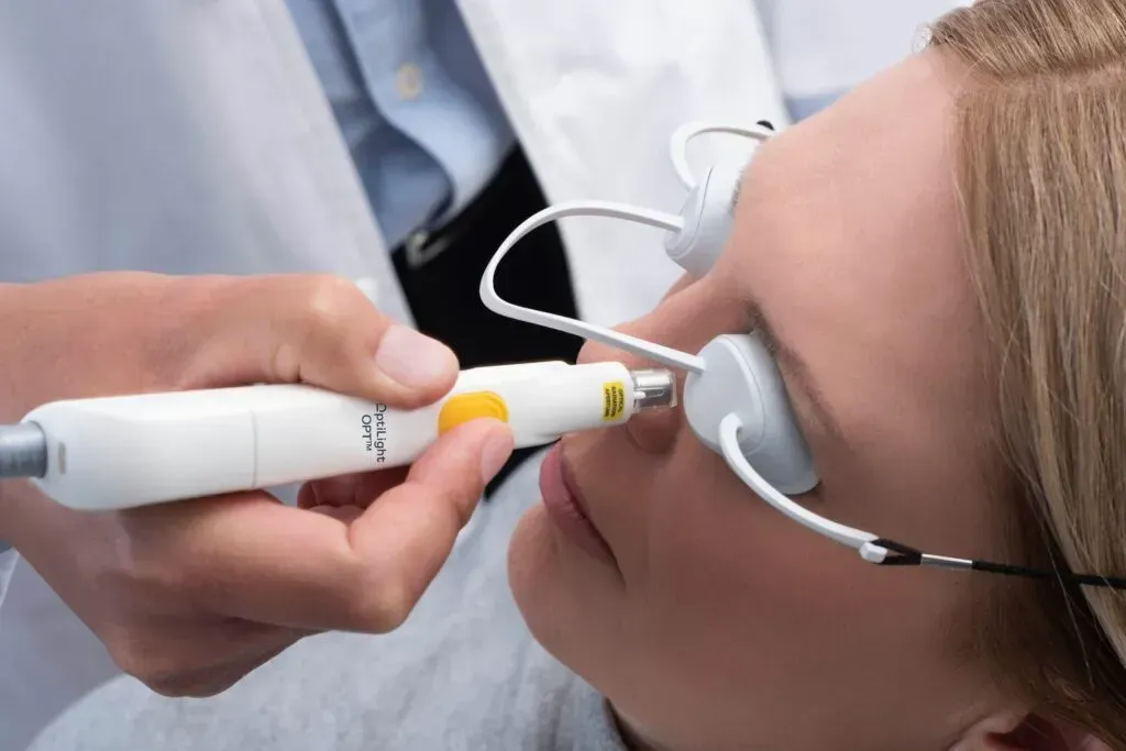 A clinician uses a handheld laser device on a patient wearing protective eyewear during a dermatological procedure.