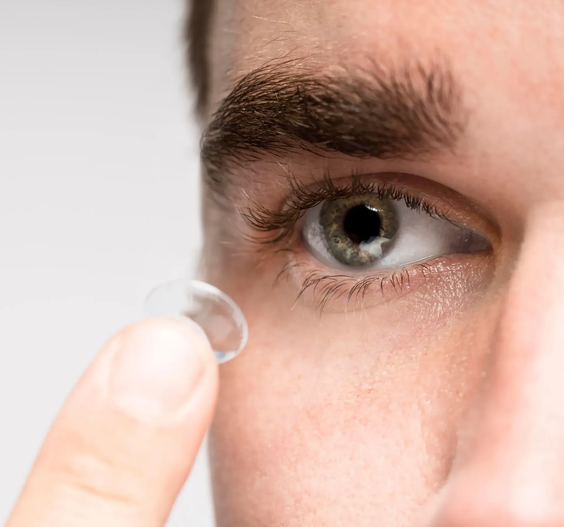 A close-up view of a person preparing to insert a clear contact lens into their eye using their fingertip.