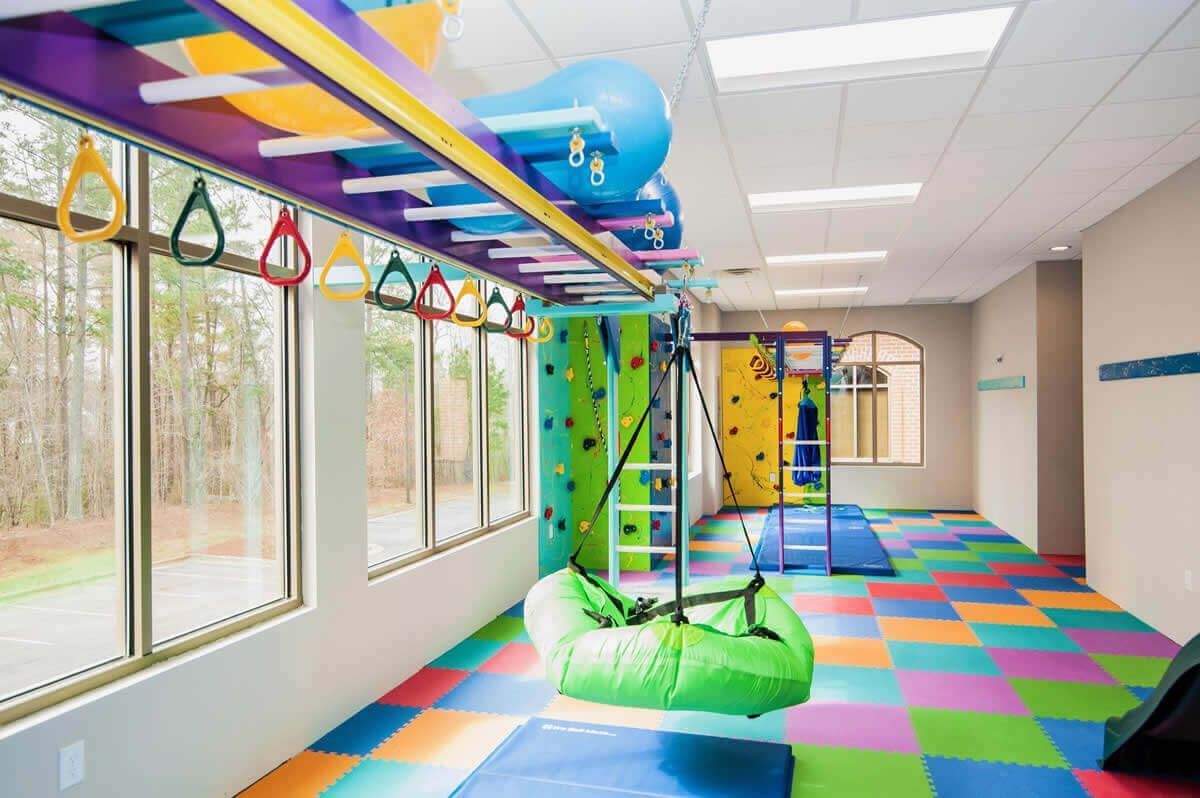 Colorful indoor playroom with climbing equipment, slides, and foam floor tiles by large windows