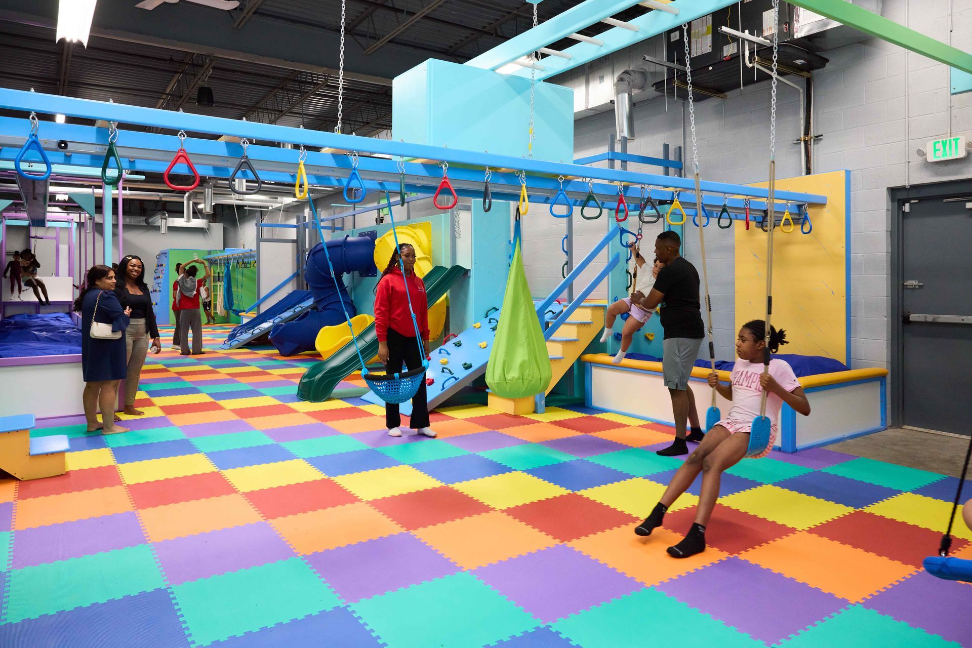 Children playing on a colorful indoor obstacle course with ramps, nets, and padded flooring.