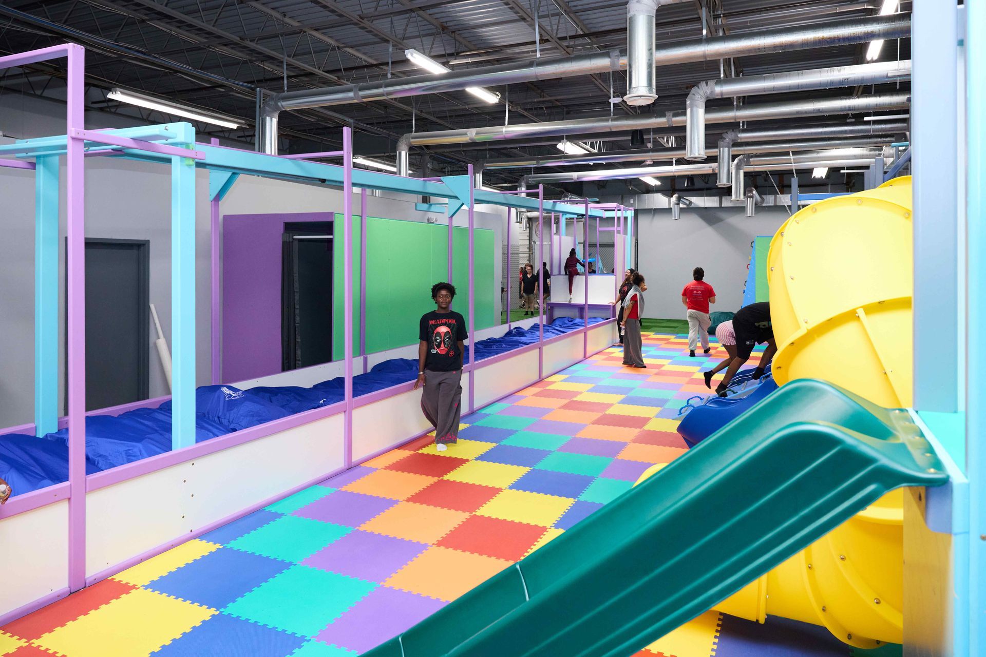Colorful indoor play area with children on a checkerboard floor and a slide in the foreground