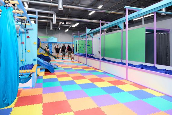 Colorful indoor play area with rainbow floor tiles, blue climbing equipment, and children in the distance