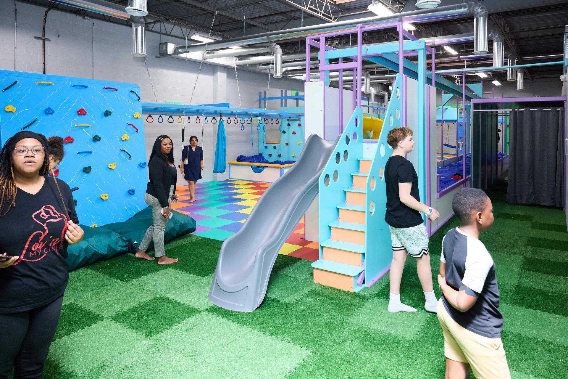 Indoor children’s play area with a slide, climbing structure, and several kids playing on colorful flooring