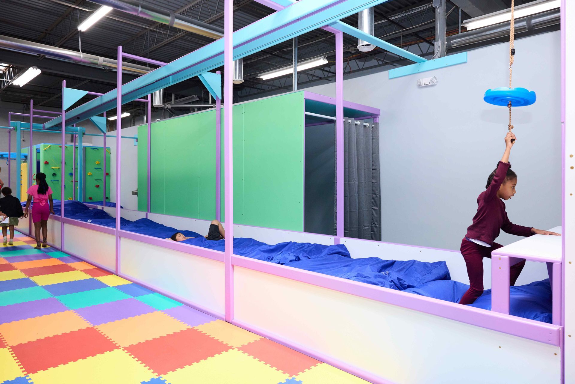 Indoor trampoline play area with colorful foam floor and children using hanging ropes and platforms