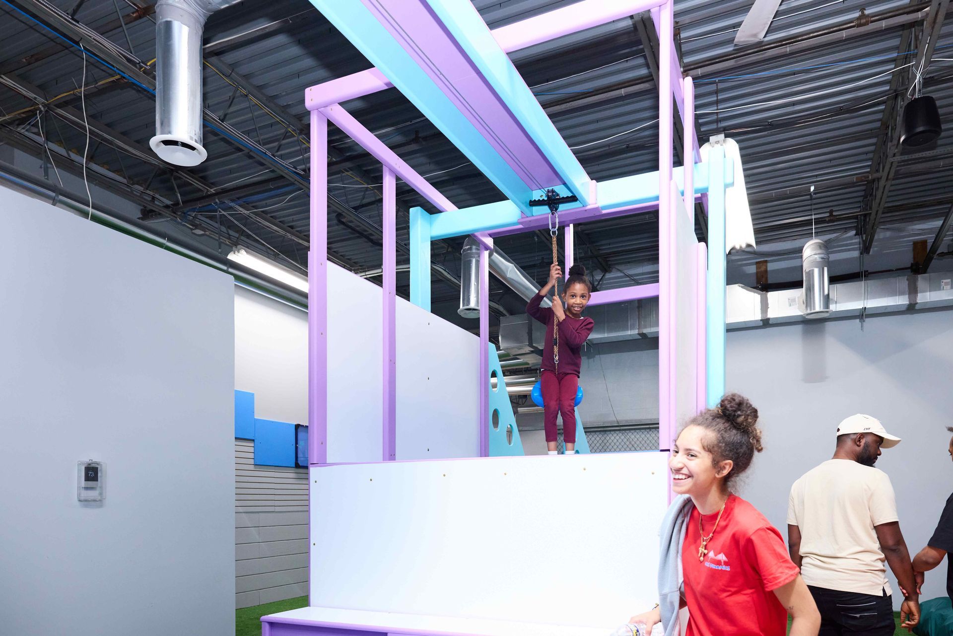 People on a colorful indoor playground with pastel rails and slides under a metal ceiling