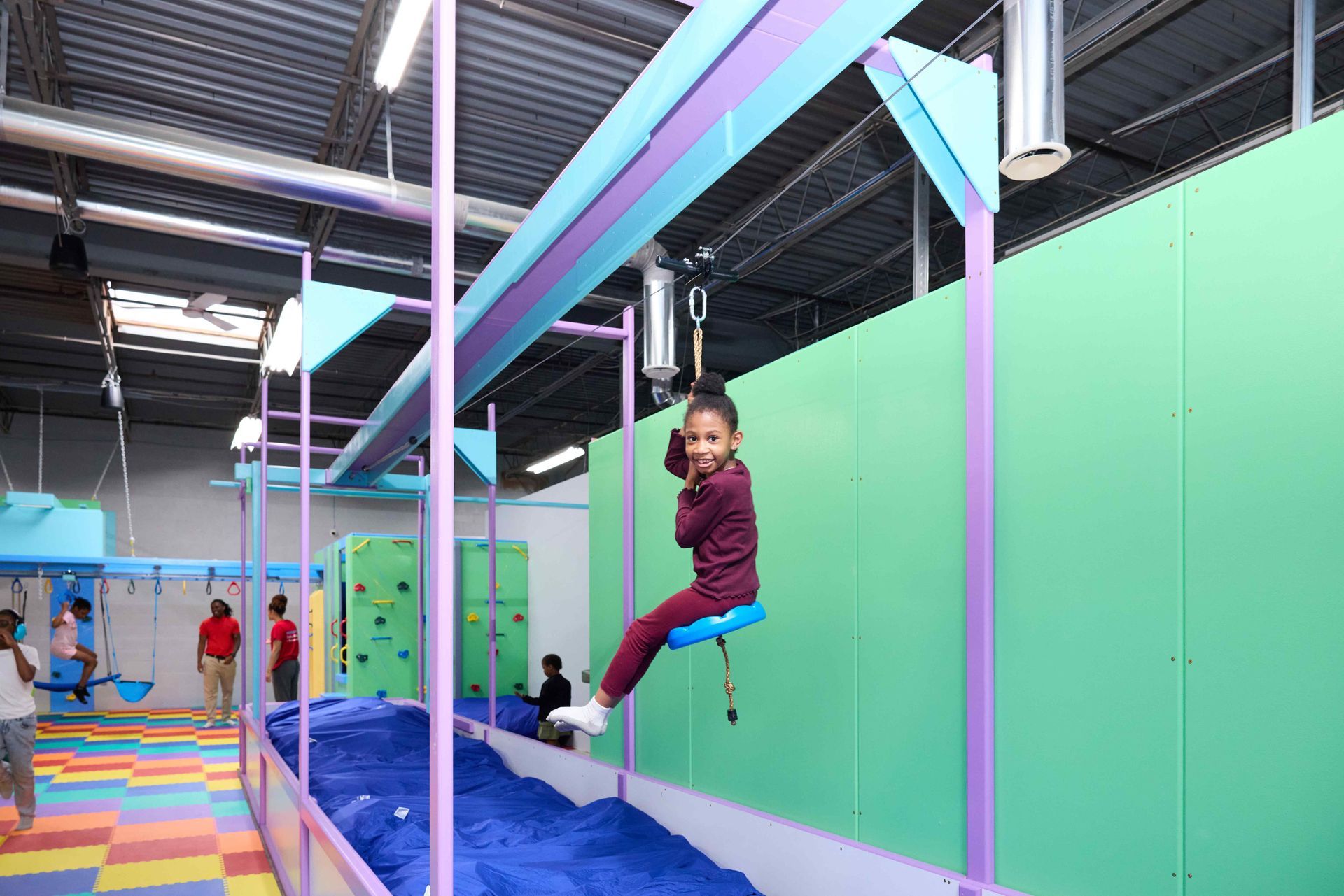 Child swinging on an indoor trampoline course with blue pads and colorful beams