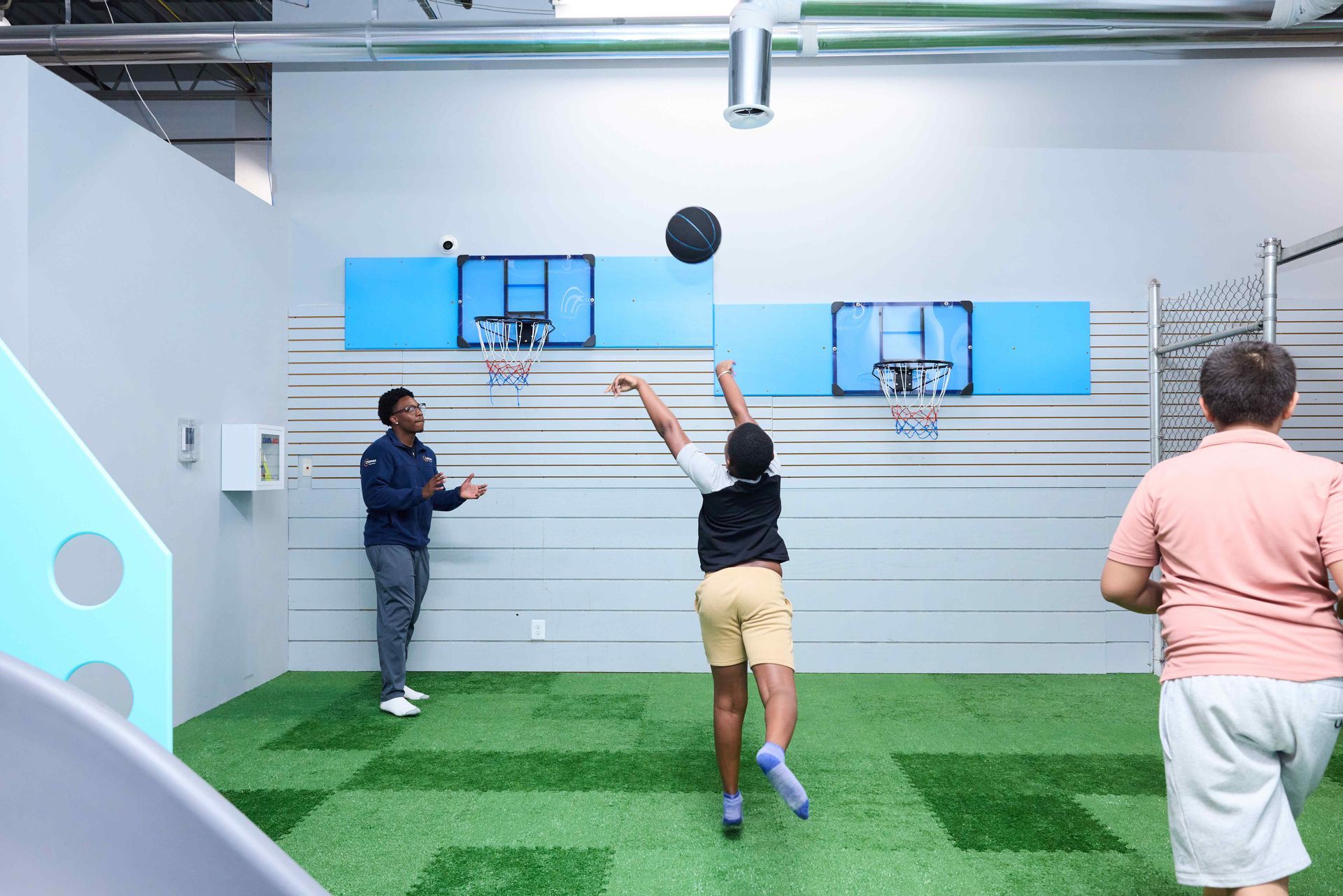 People playing basketball indoors, one person shooting toward two wall-mounted hoops.