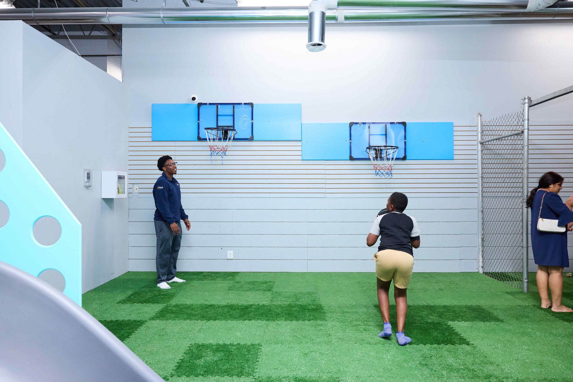 People on an indoor turf field practicing near a wall-mounted basketball hoop.