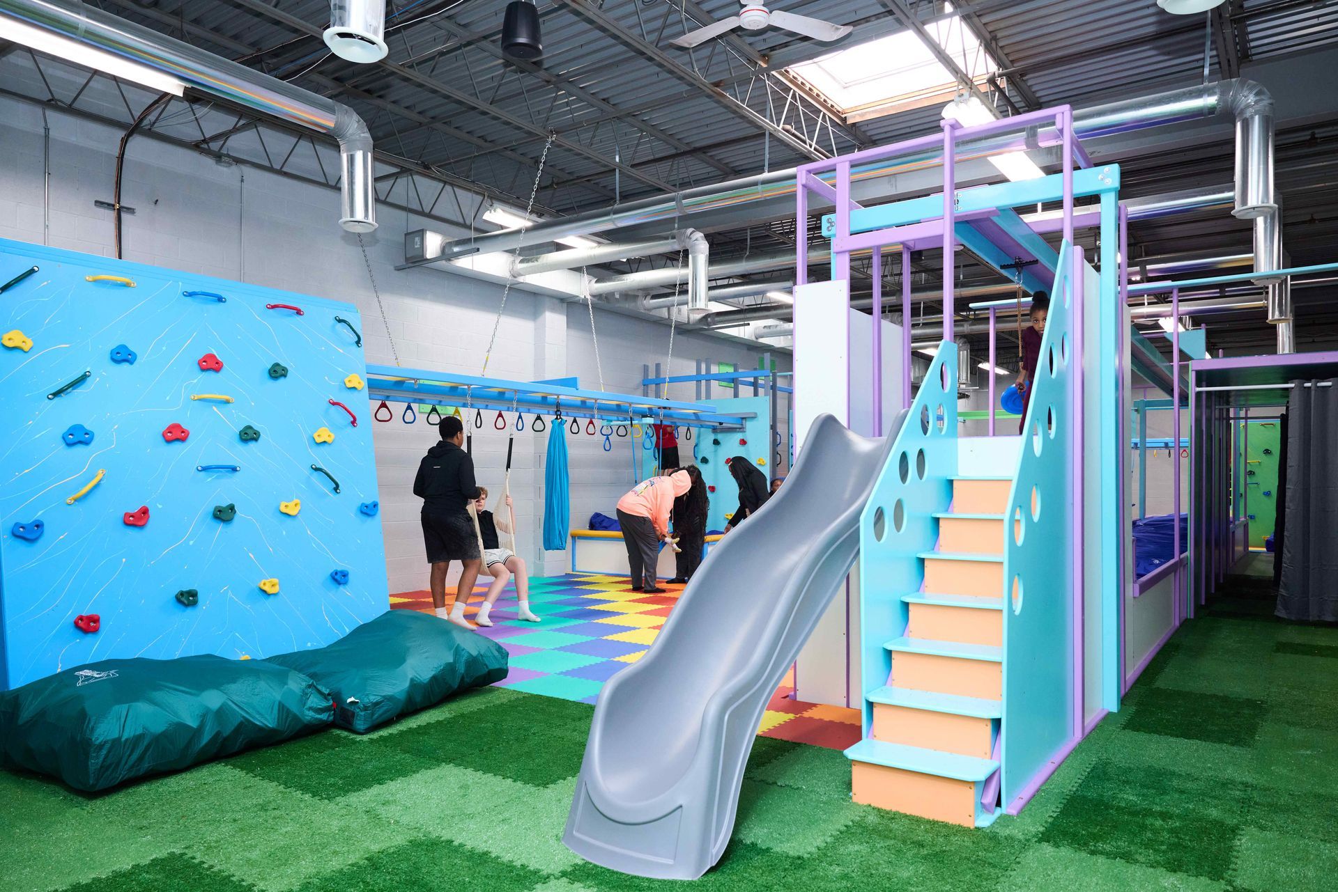 Indoor kids’ obstacle course with slide, climbing wall, and rainbow stairs in a gym