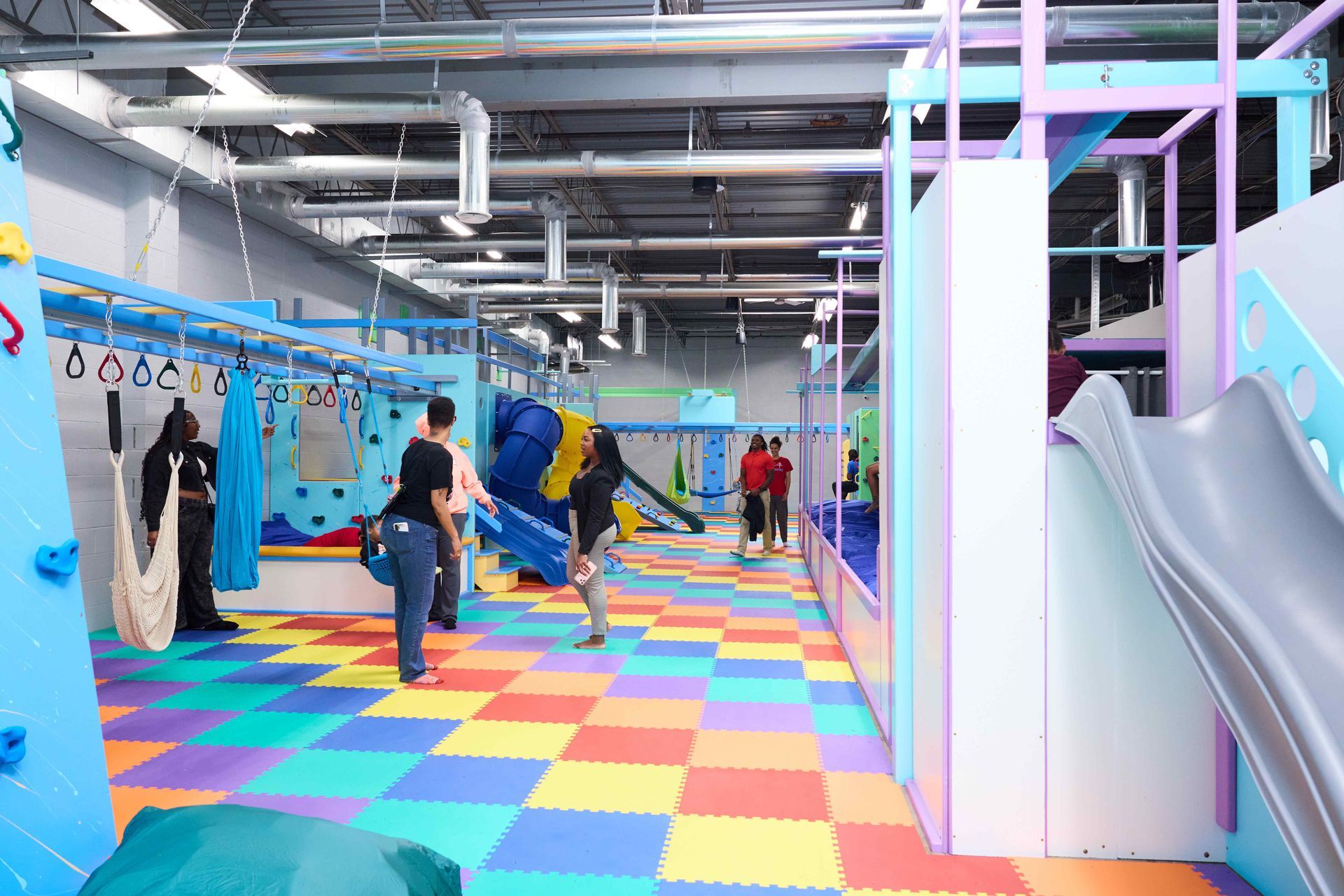 Bright indoor playground with colorful tile floor, slides, and a few people walking inside