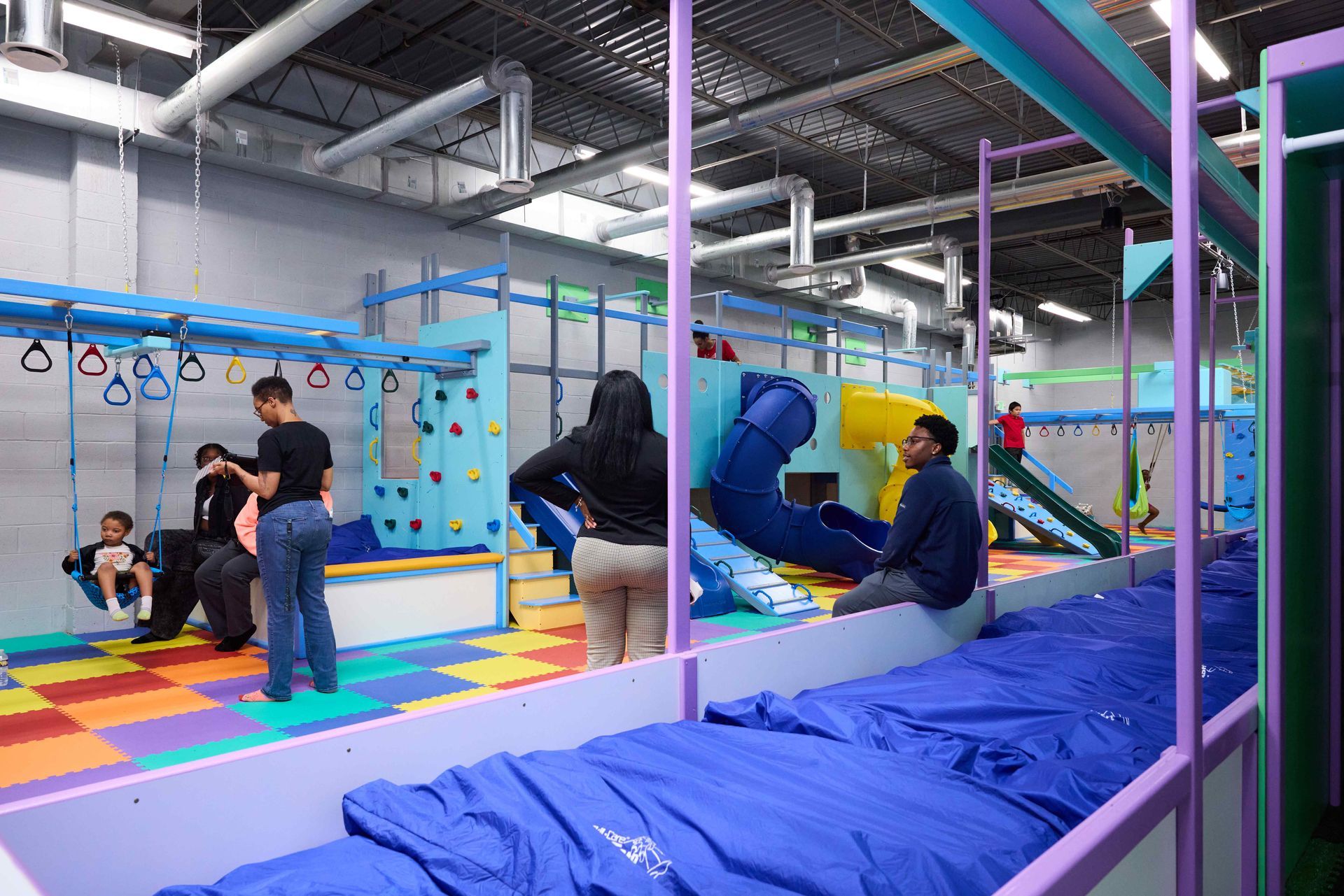 Indoor playground with children climbing on colorful equipment and a blue foam pit