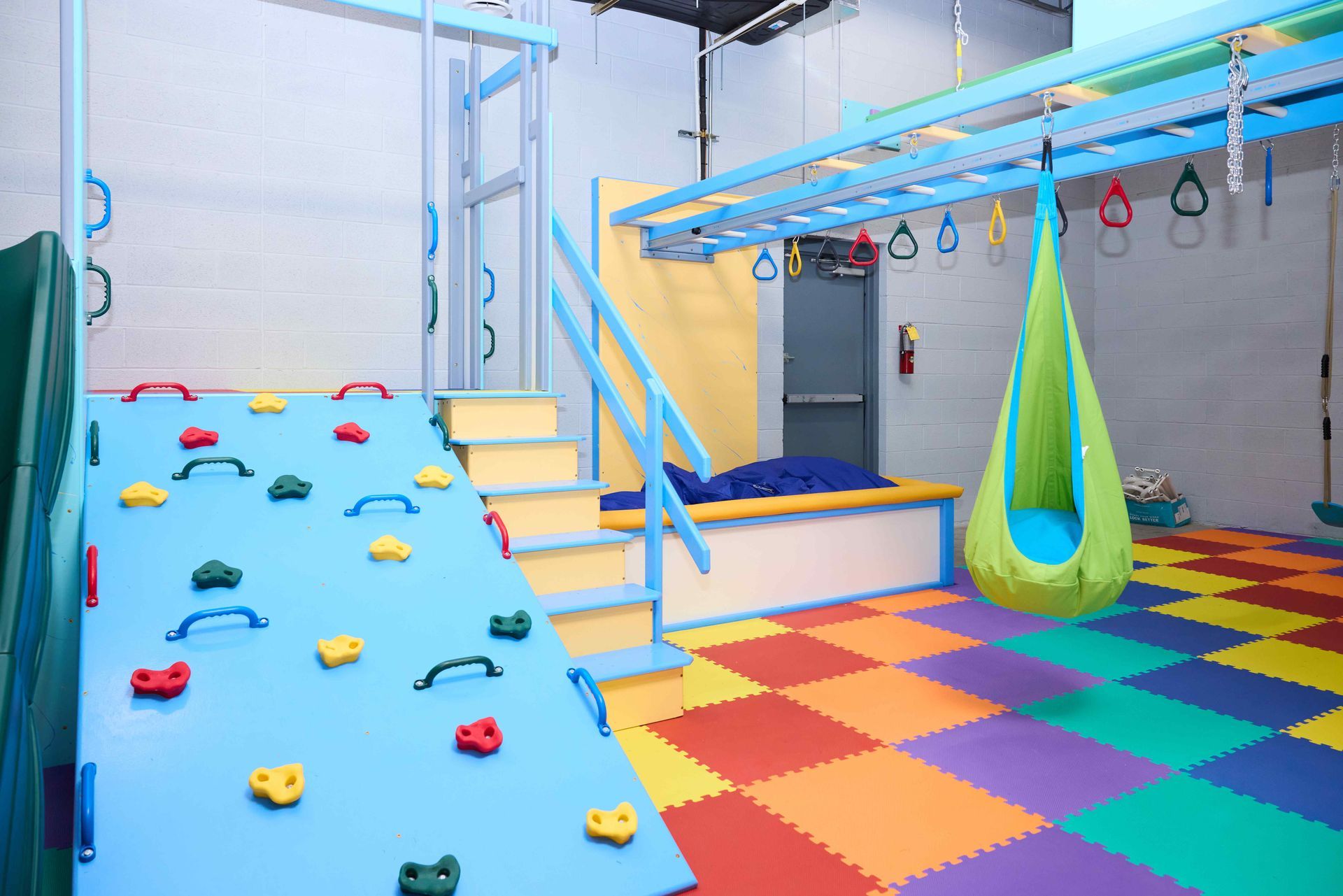 Indoor playground with a blue climbing ramp, hanging green swing, and colorful foam floor tiles