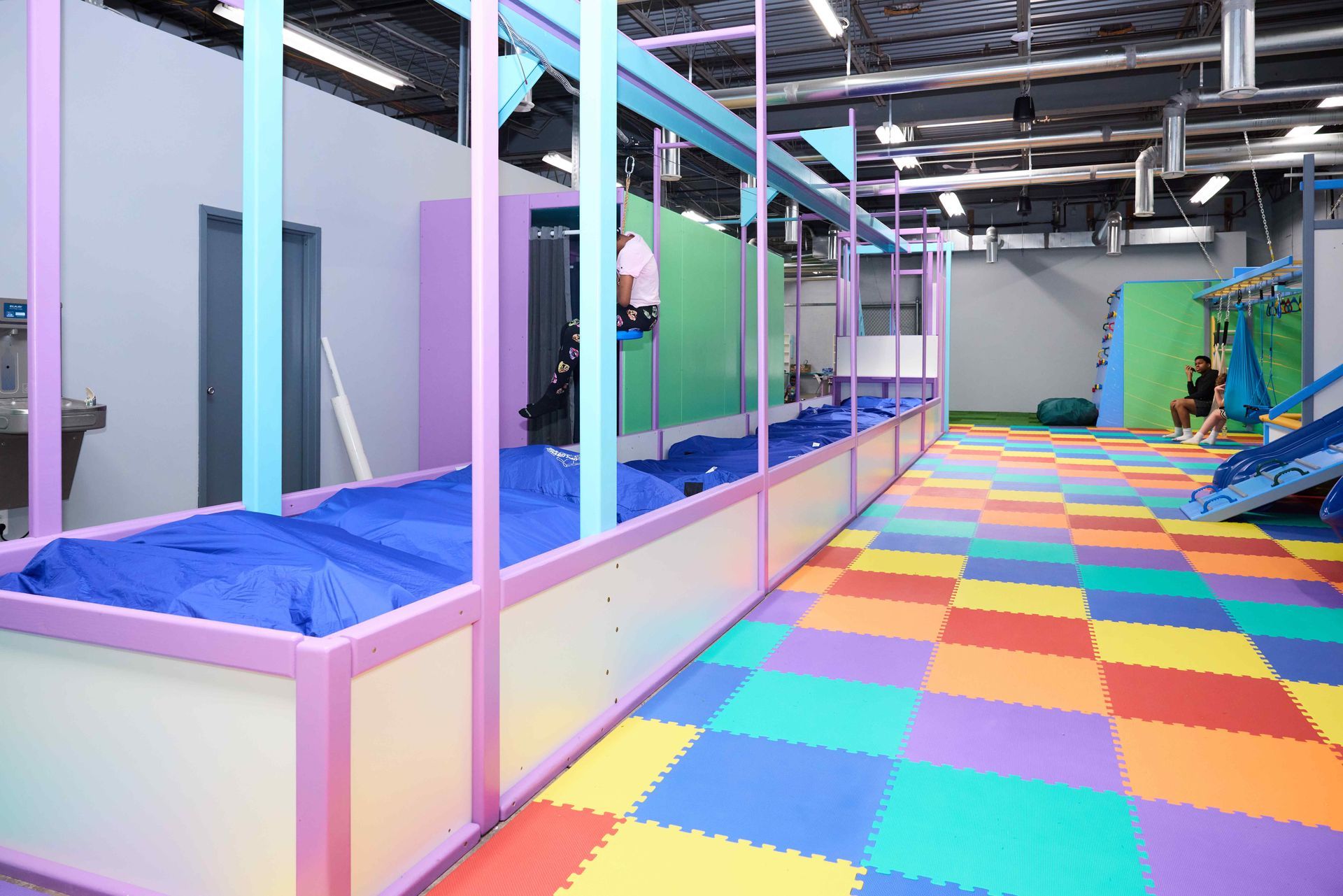Colorful indoor play area with padded mats, trampolines, and a rainbow foam floor