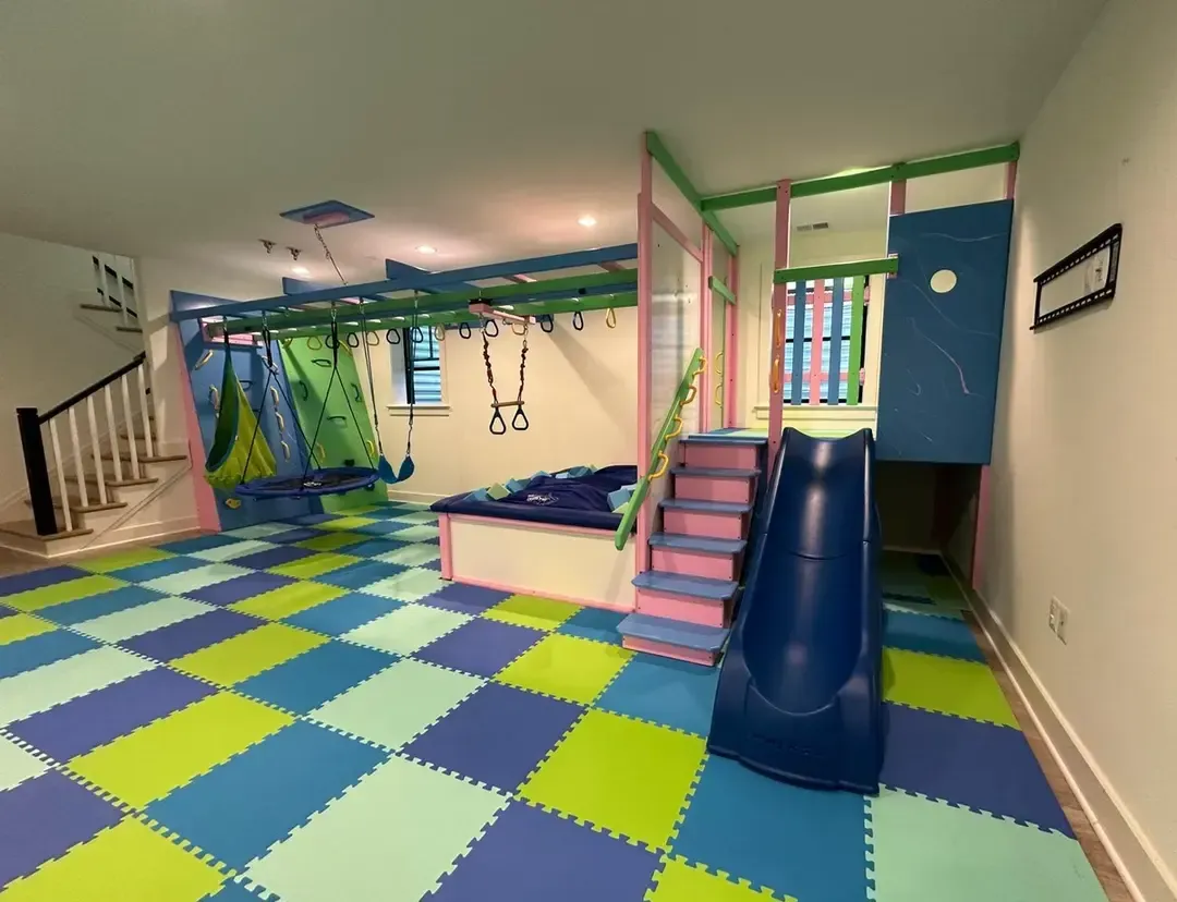 Colorful indoor playroom with foam floor tiles, slides, swings, and climbing structures