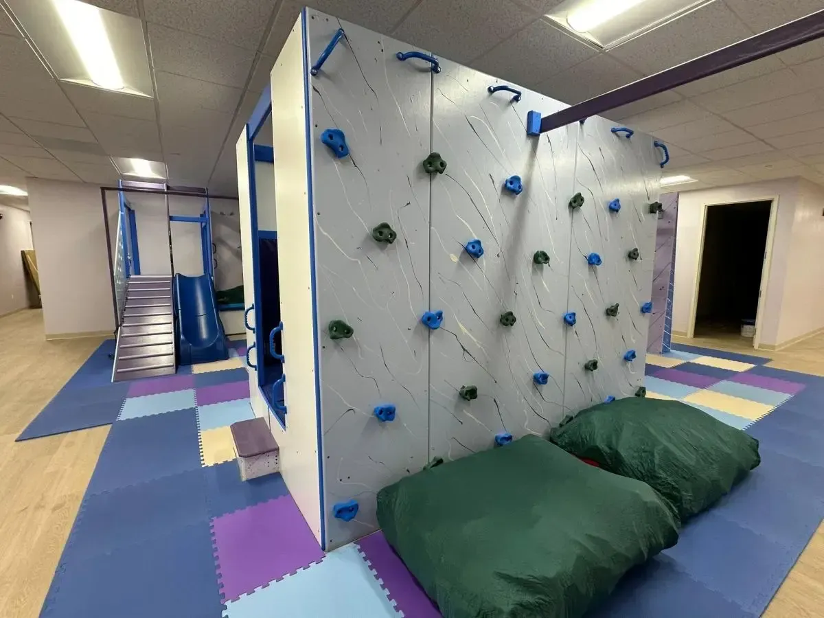 Indoor playroom with climbing wall, green crash mats, and colorful padded flooring