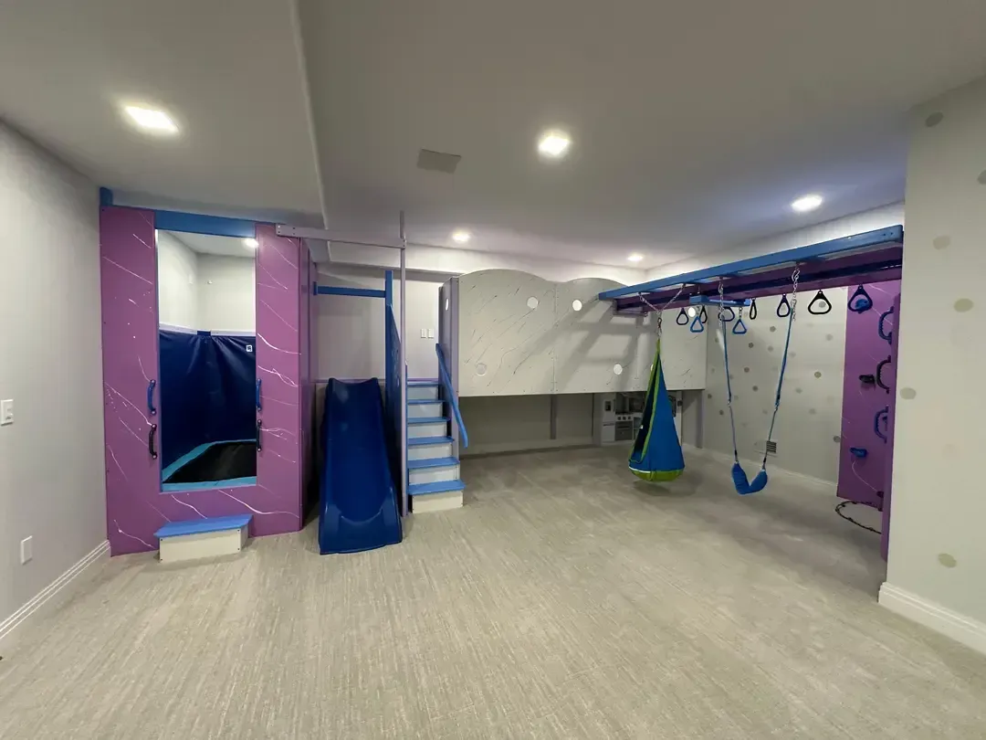 Indoor playroom with climbing and hanging sensory equipment in purple and blue.