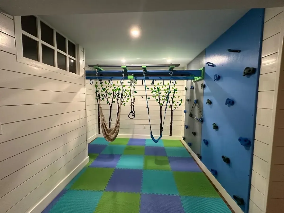 Indoor obstacle course with hanging ropes, blue climbing wall, and green-blue padded floor tiles