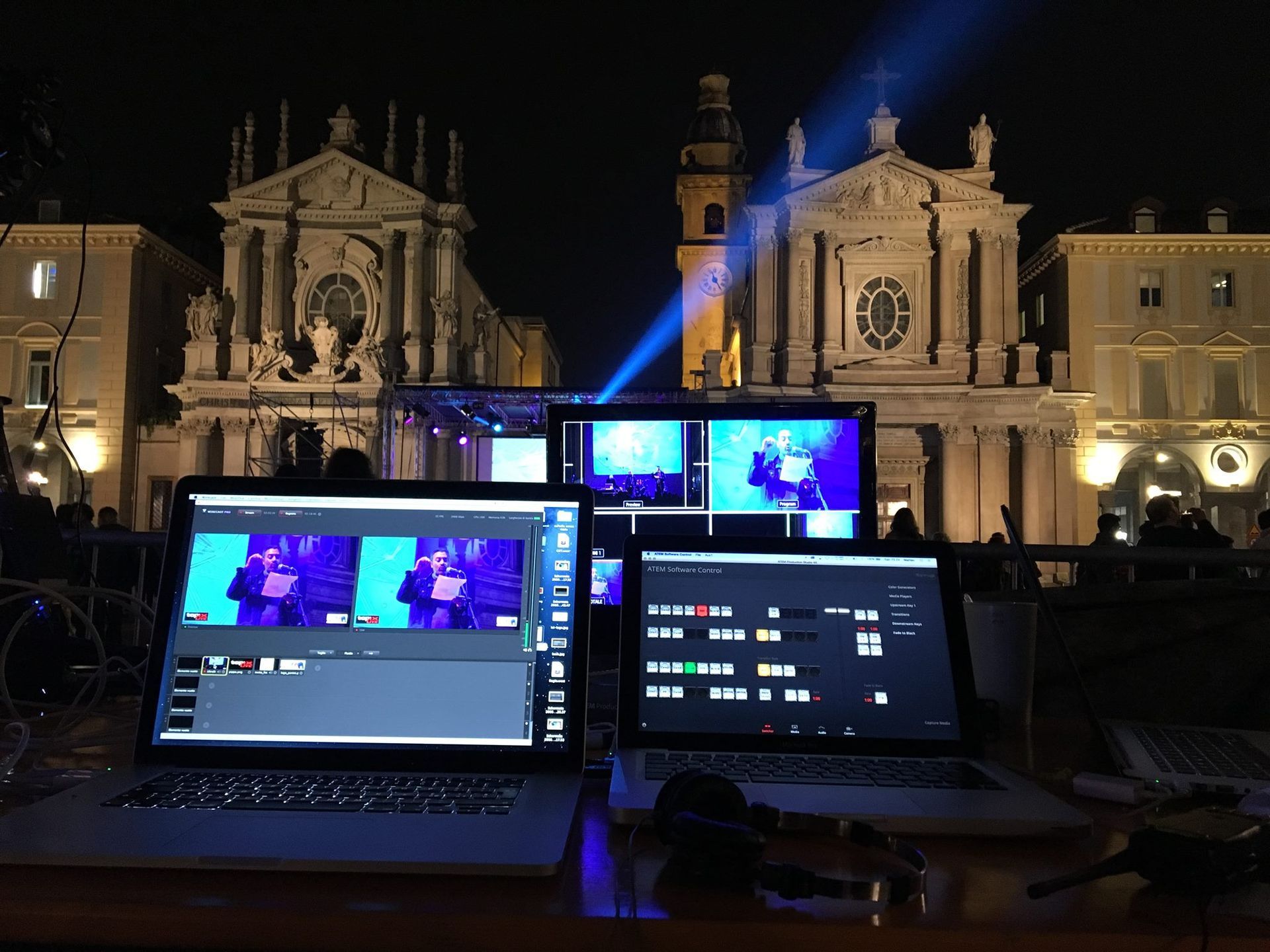 Computer portatili con software di editing video, palco e schermi di fronte alla cattedrale illuminata di notte.