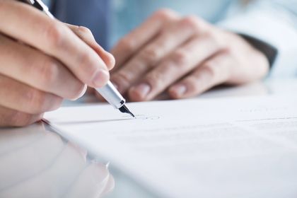 Mani che tengono una penna sopra un documento vuoto su una scrivania