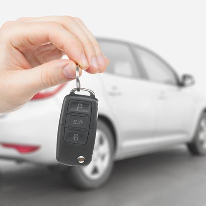 Una mano che tiene un telecomando nero per auto davanti a un'auto bianca
