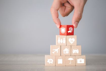 Una mano posiziona un cubo rosso sopra una piramide di blocchi di legno con icone sanitarie bianche.