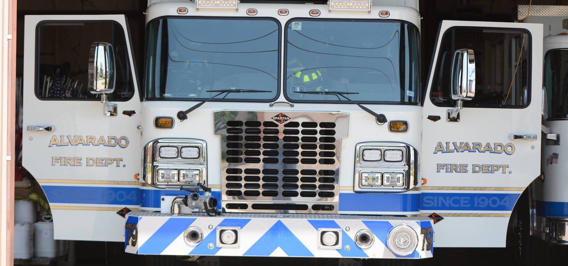 A white and blue Alvarado fire truck is parked in a garage