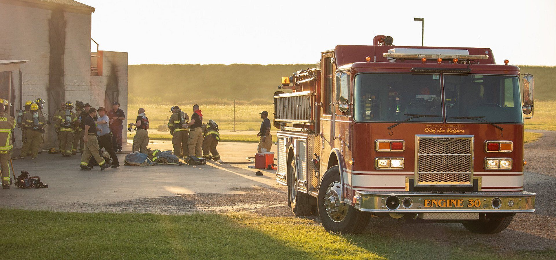 A fire truck is parked in front of a group of firefighters.