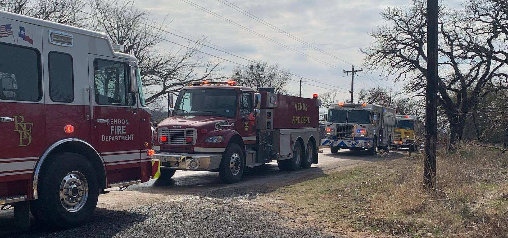 A row of fire trucks are parked on the side of a dirt road.