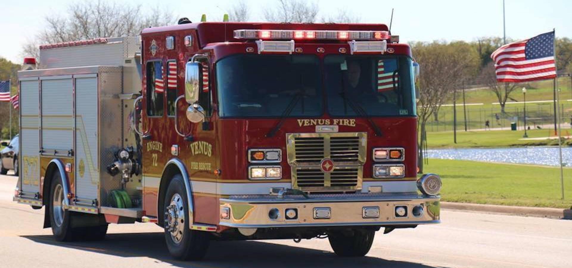 A Venus fire truck is driving down a street with American flags in the background.