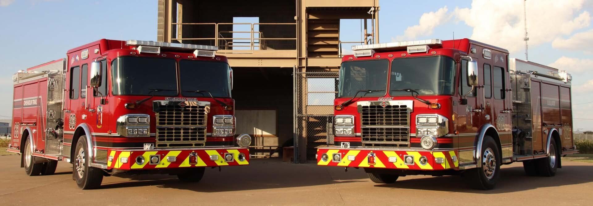 Two fire trucks are parked next to each other in front of a training burn tower.