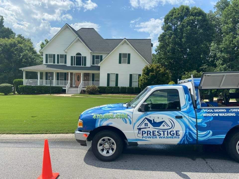 Blue Prestige truck parked in front of a white house with an orange traffic cone in the foreground