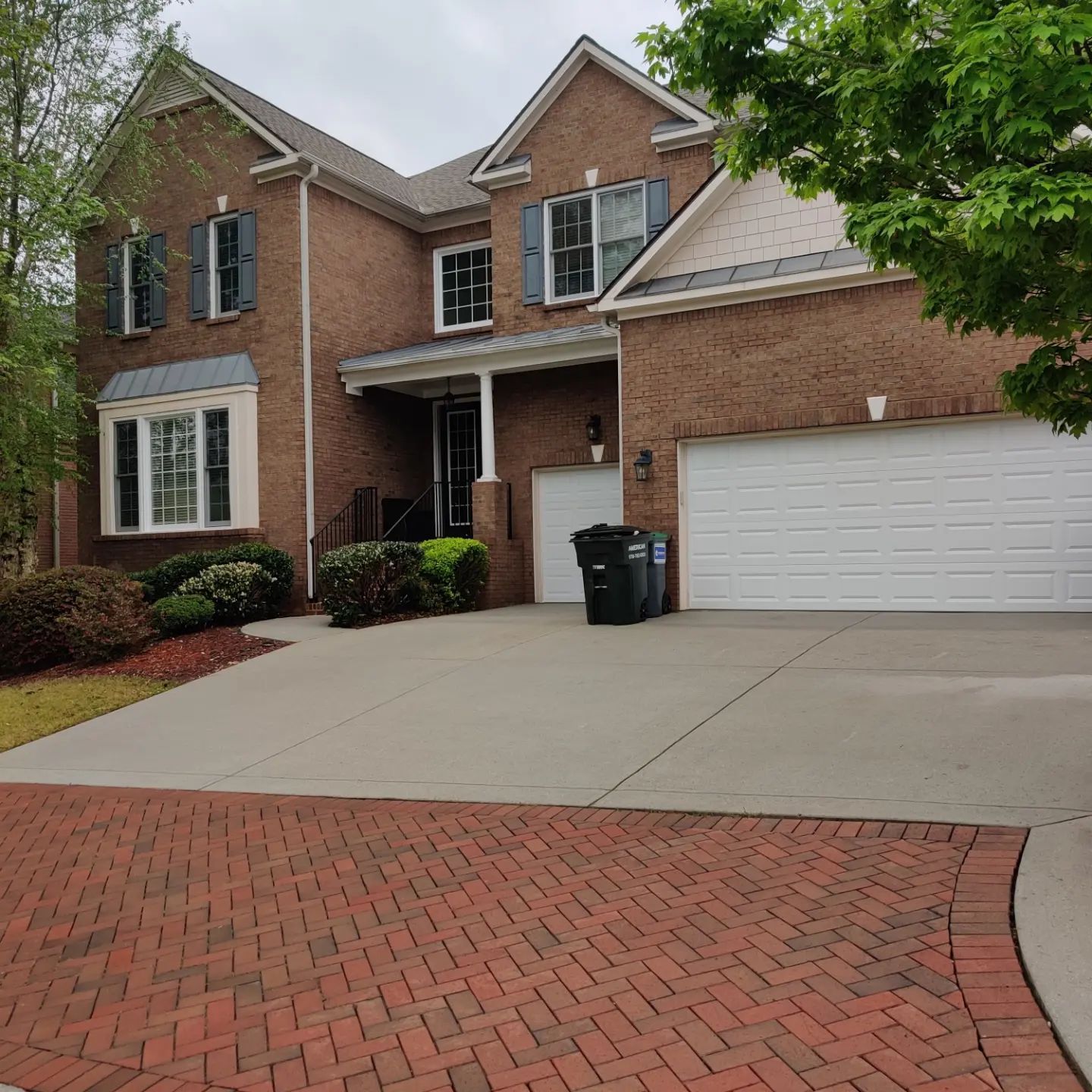 Brick suburban house with white garage, red driveway, and front porch under cloudy skies