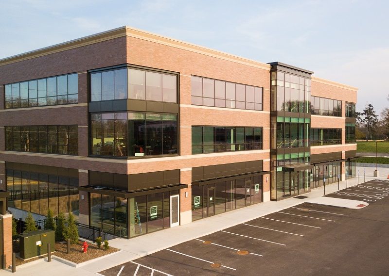 Modern three-story office building with dark glass windows and a parking lot under clear sky