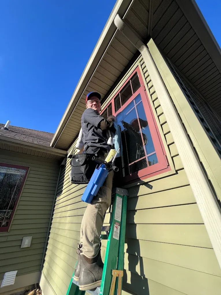 Man cleaning a window on a house exterior using a ladder